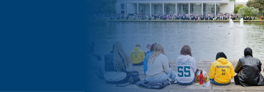A group of new student sitting in front of the lake, watching a graduation ceremony